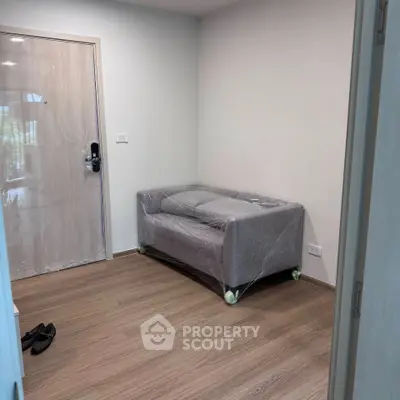 Cozy small living room with a new sofa wrapped in plastic, wooden flooring, and a secure door.