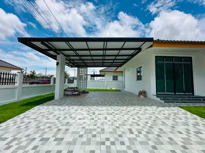 Modern single-story house with spacious driveway and carport, featuring sleek design and lush green lawn.