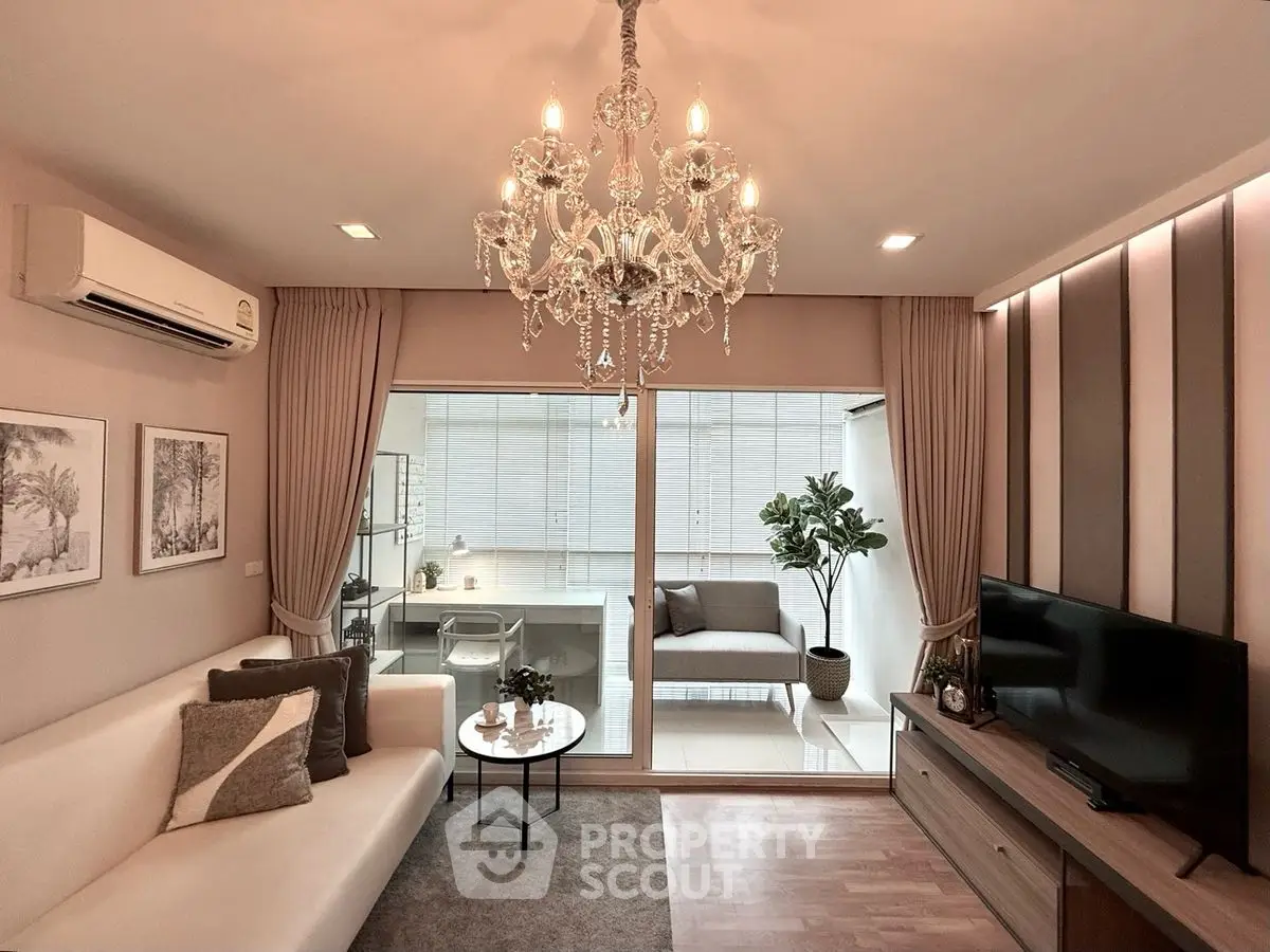 Elegant living room with chandelier and modern decor, featuring a cozy seating area and large windows.
