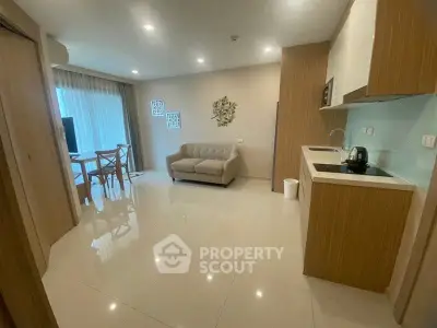 Modern open-layout living room with kitchen, featuring sleek furniture and bright lighting.