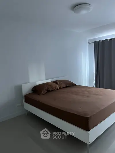 Modern minimalist bedroom with sleek white bed and brown bedding, featuring natural light from large window.