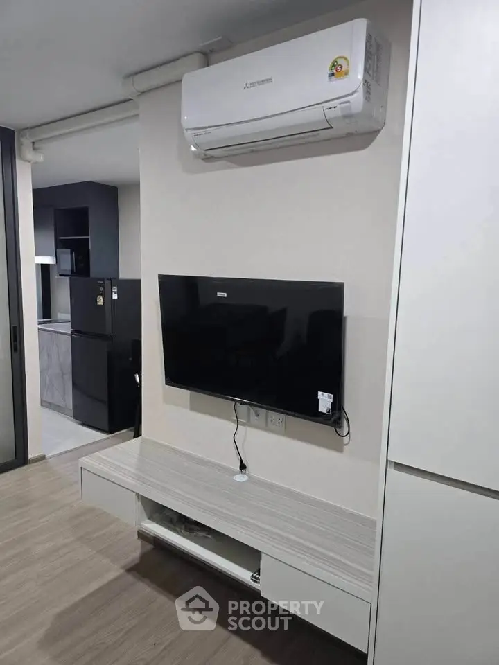 Modern living room with wall-mounted TV and air conditioning, featuring sleek furniture and open kitchen view.