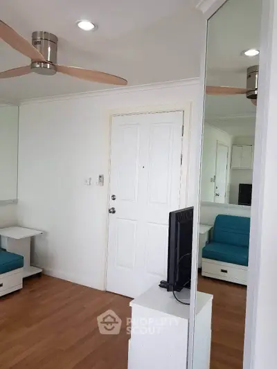 Modern living room with wooden flooring and ceiling fan, featuring a sleek white door and mirrored wall.