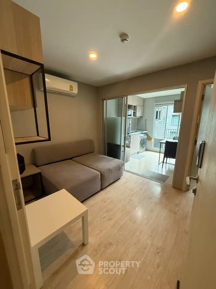 Modern living room with open layout to kitchen, featuring sleek furniture and wooden flooring.
