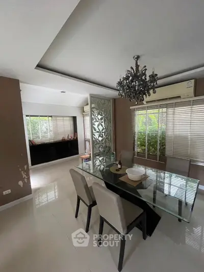 Elegant dining room with glass table and chandelier, featuring large windows and modern decor.