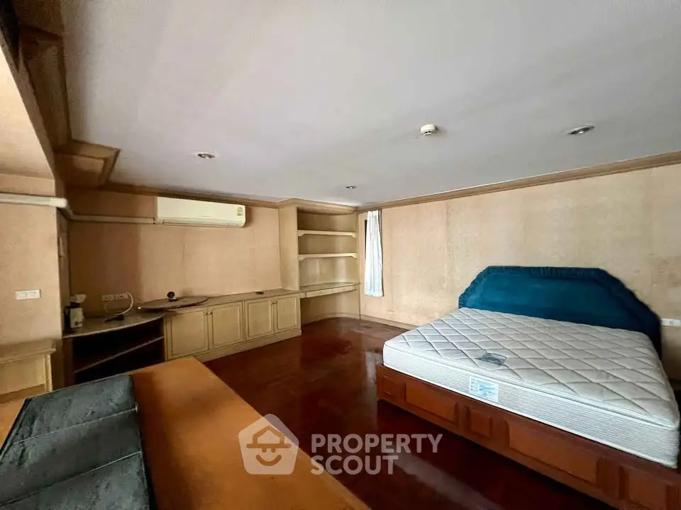 Spacious bedroom with built-in shelves and air conditioning, featuring a large bed and wooden flooring.