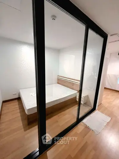 Modern bedroom with glass partition and wooden flooring in a stylish apartment.