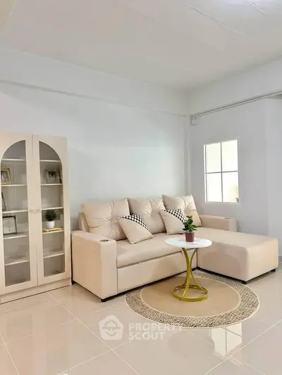 Modern living room with beige sofa, stylish cabinet, and chic round table in bright interior.