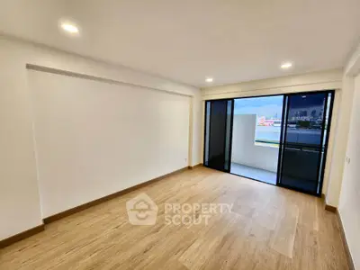 Spacious empty room with wooden flooring and balcony access