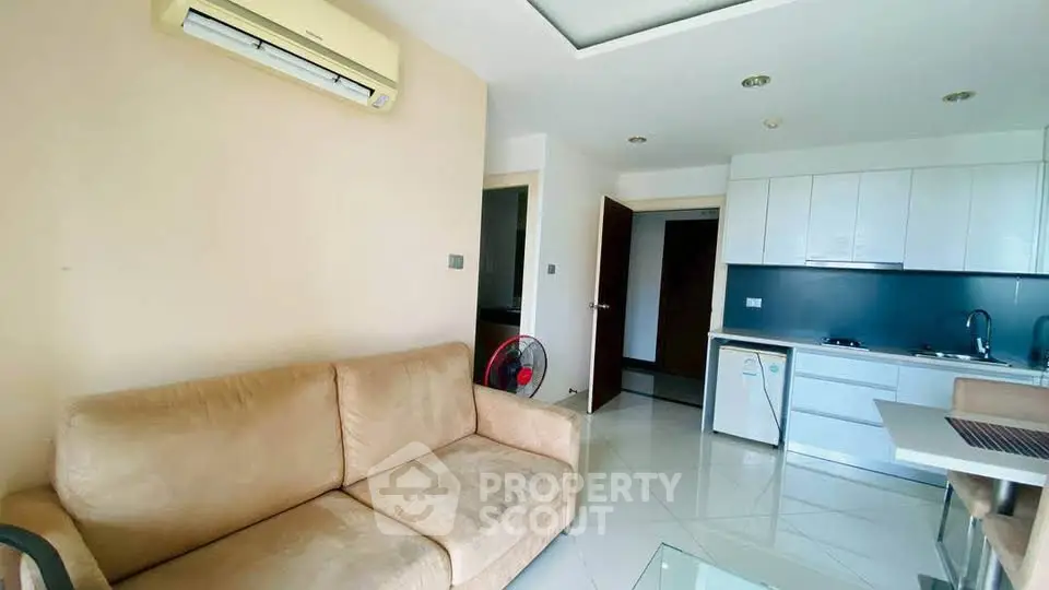 Modern living room with beige sofa and compact kitchen in open layout apartment.