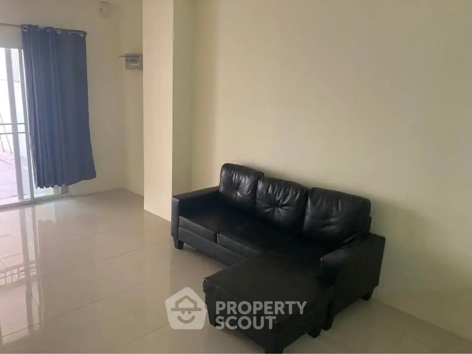 Spacious living room with sleek black leather sofa and large windows for natural light.