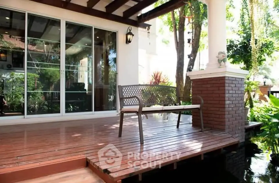 Charming patio with wooden deck overlooking lush garden and pond, perfect for relaxation.
