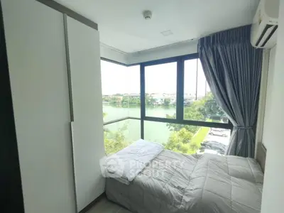 Cozy bedroom with large windows offering stunning river view and modern furnishings.