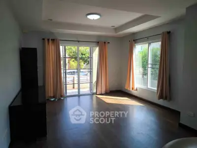 Spacious living room with large windows and natural light, featuring elegant curtains and modern flooring.