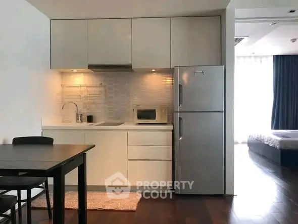 Modern kitchen with sleek cabinetry and stainless steel fridge in open-plan apartment.