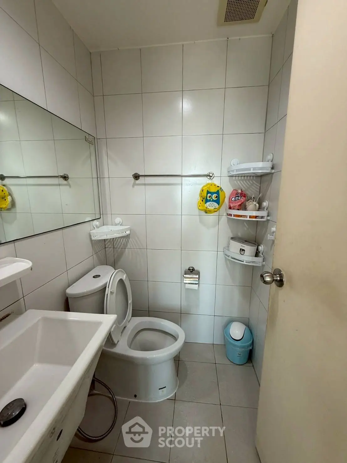 Compact bathroom with modern fixtures and tiled walls, featuring a toilet, sink, and storage shelves.