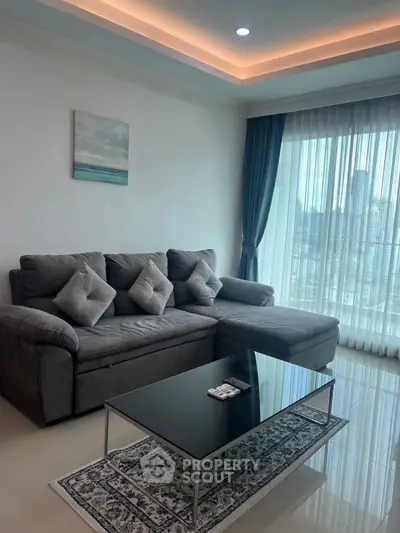 Modern living room with plush gray sofa and city view through large windows.