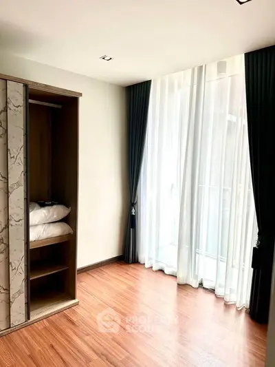 Bright bedroom with wooden flooring and large window with elegant curtains.
