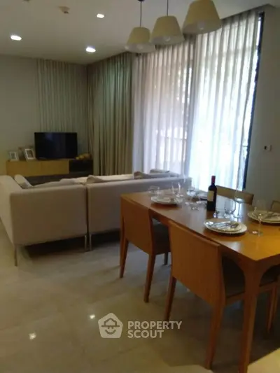 Elegant living room with dining area, featuring modern furniture and natural light through large windows.