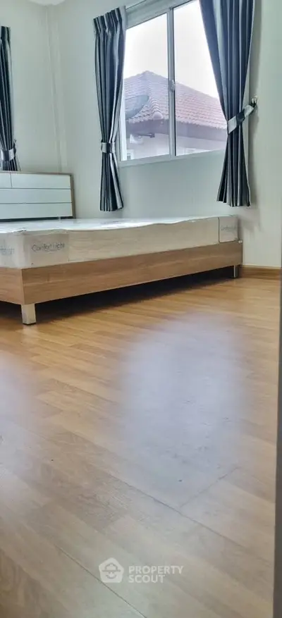 Spacious bedroom with wooden flooring and large window offering natural light