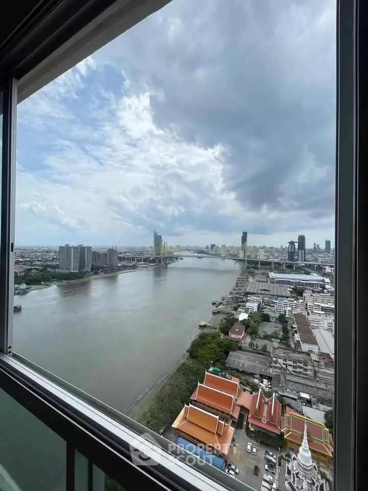 Stunning river view from high-rise apartment window with cityscape and cloudy sky.
