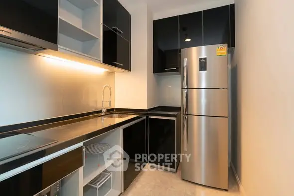 Modern kitchen with sleek black cabinets and stainless steel appliances in a contemporary apartment.