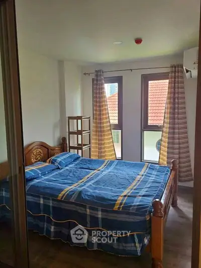 Cozy bedroom with wooden bed frame and large windows offering natural light.