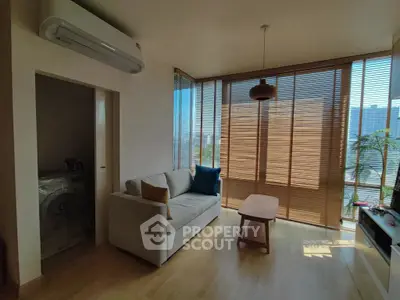 Modern living room with large windows and natural light, featuring a cozy sofa and wooden blinds.