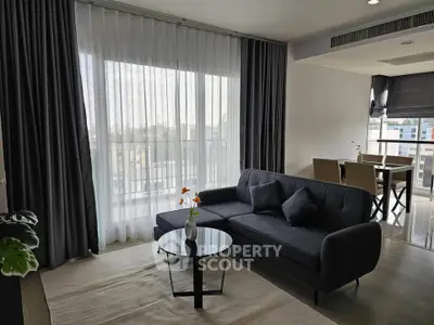 Modern living room with elegant sofa and dining area, featuring large windows and stylish decor.