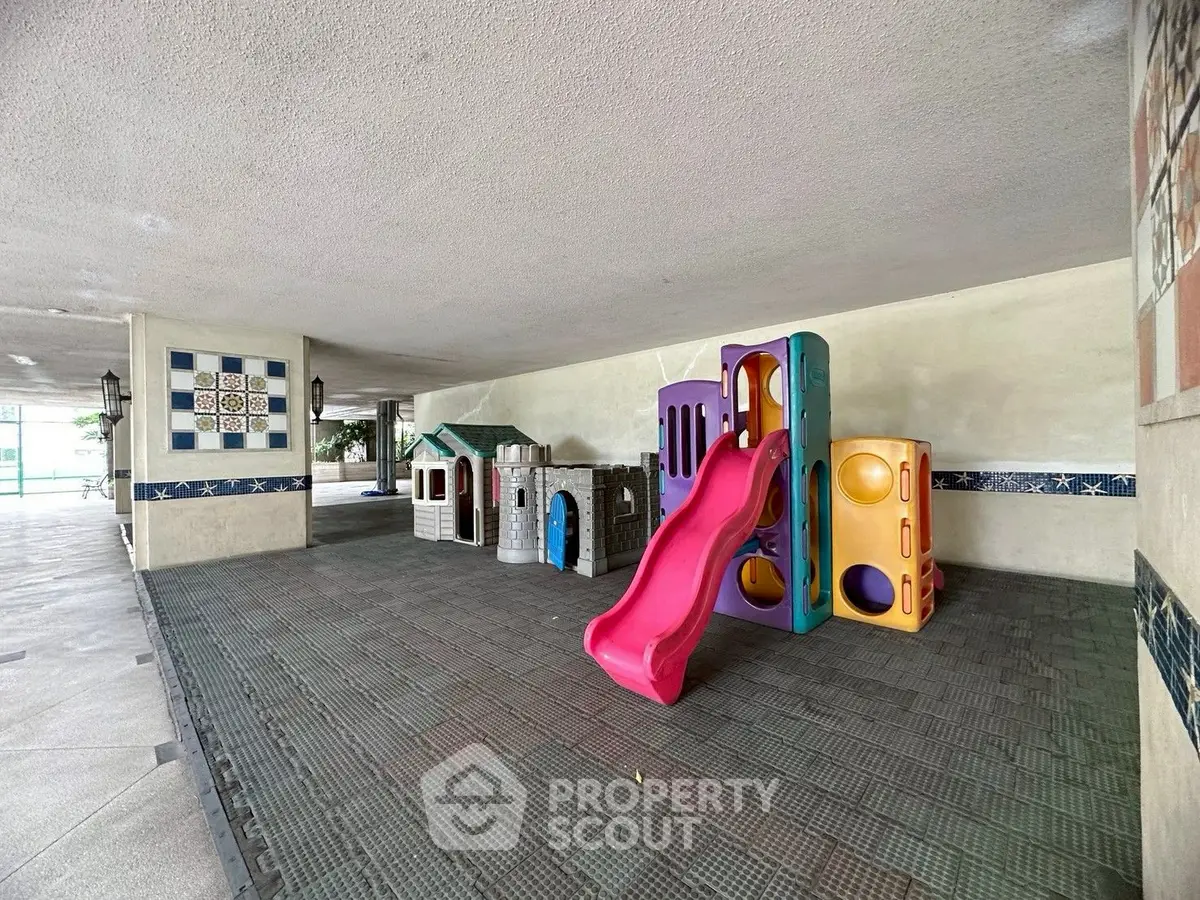 Spacious covered play area with colorful playground equipment in a residential complex.