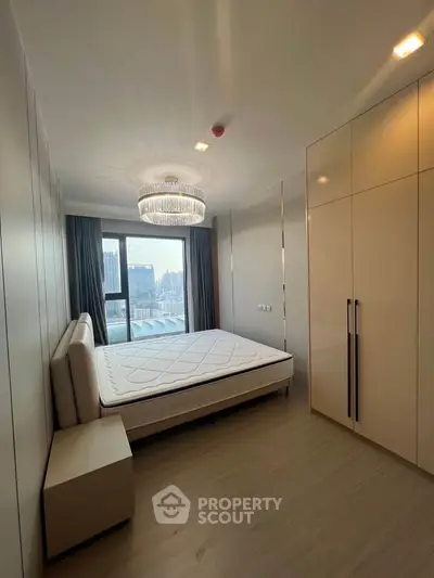 Modern bedroom with city view, elegant chandelier, and spacious wardrobe in a high-rise apartment.