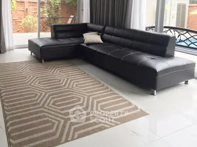 Modern living room with sleek black sectional sofa and geometric rug near poolside view.