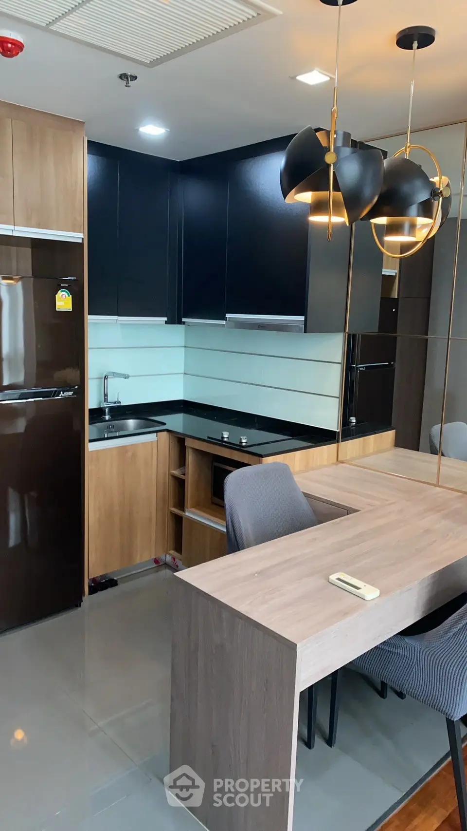Modern kitchen with sleek black cabinets and wooden accents, featuring a built-in oven and stylish lighting.