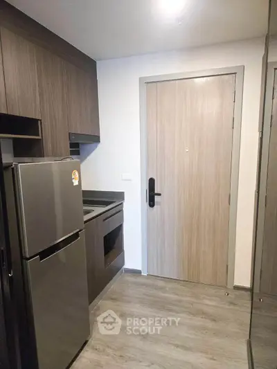 Modern compact kitchen with sleek wooden cabinets and stainless steel fridge