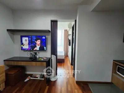 Modern apartment interior with wooden flooring and wall-mounted TV, leading to a cozy bedroom.