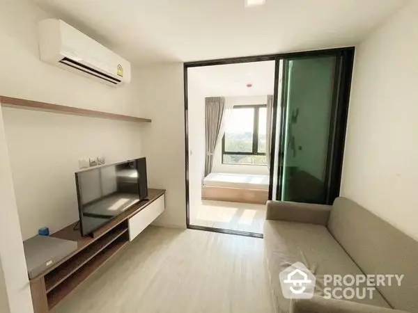 Bright and airy living room with sleek modern furniture, large windows leading to a sunny balcony, and a wall-mounted flat-screen TV.