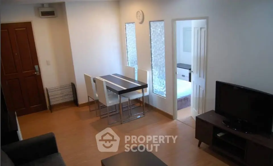 Modern living room with dining area and view into bedroom, featuring sleek furniture and wooden flooring.