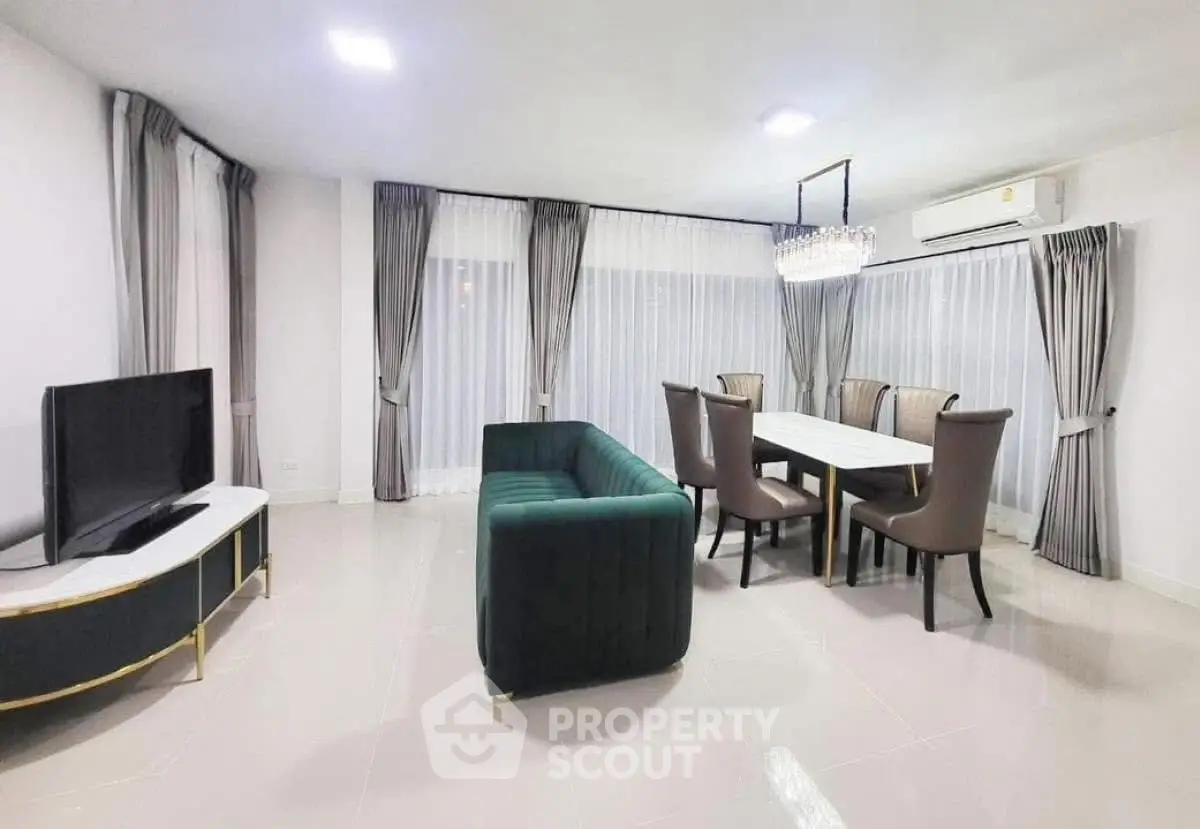 Elegant living room with modern furniture and dining area, featuring a stylish chandelier and large windows.