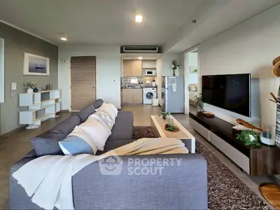 Modern living room with stylish decor and open kitchen layout, featuring a cozy gray sofa and wall-mounted TV.