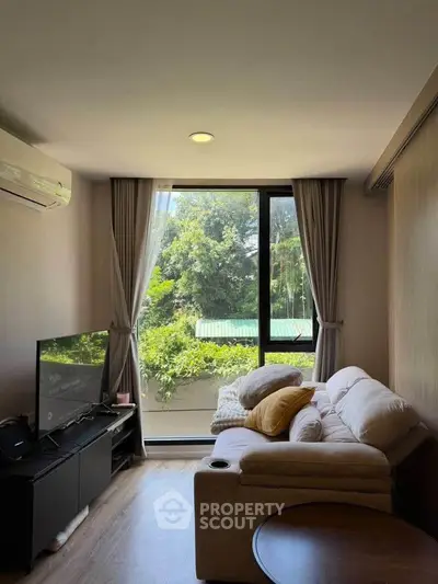 Cozy living room with large window and lush greenery view, featuring a comfortable sofa and modern TV setup.