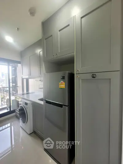 Modern kitchen with sleek cabinets, fridge, and washing machine in a bright apartment with city view.