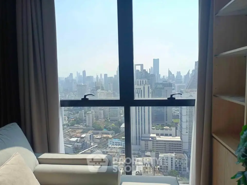 Stunning cityscape view from a high-rise apartment window with cozy seating area.