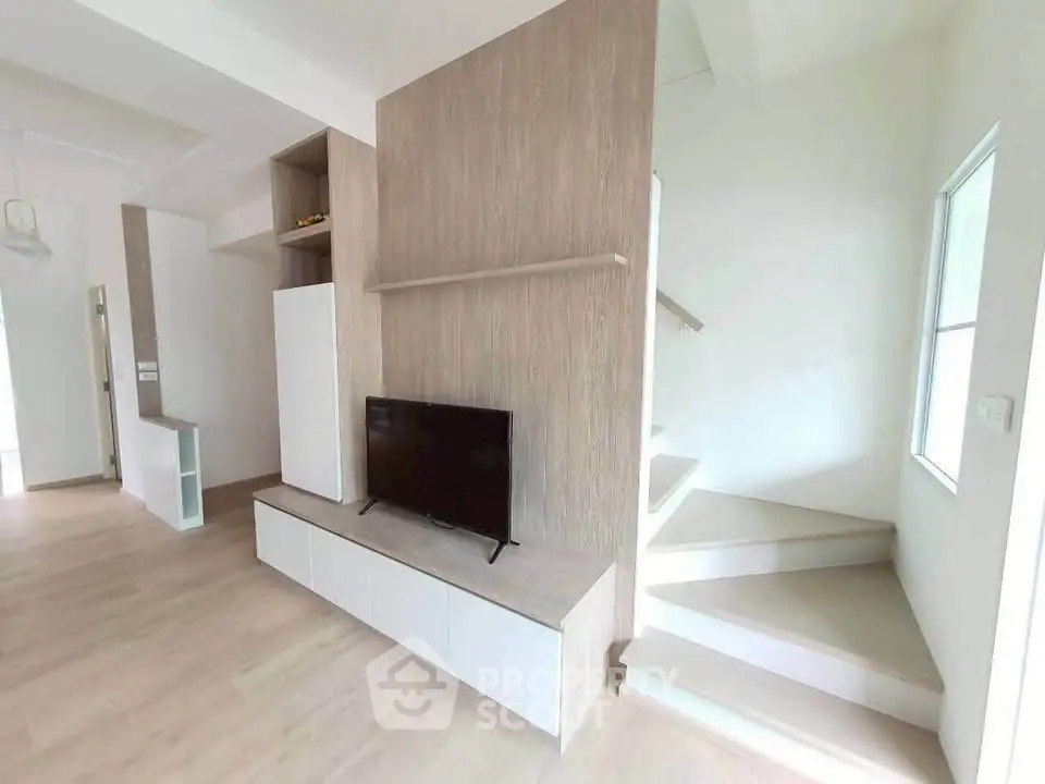 Modern living room with sleek wooden paneling and staircase, featuring a minimalist TV setup.