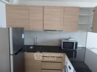 Modern kitchen with sleek cabinets, black countertop, and appliances including fridge, microwave, and washing machine.