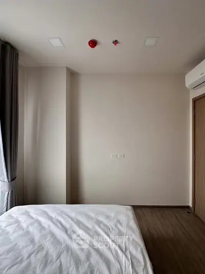 Minimalist bedroom with white bedding and wooden flooring, featuring natural light from large window.