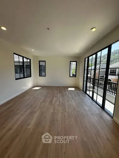 Spacious living room with large windows and wooden flooring, offering ample natural light and a serene view.