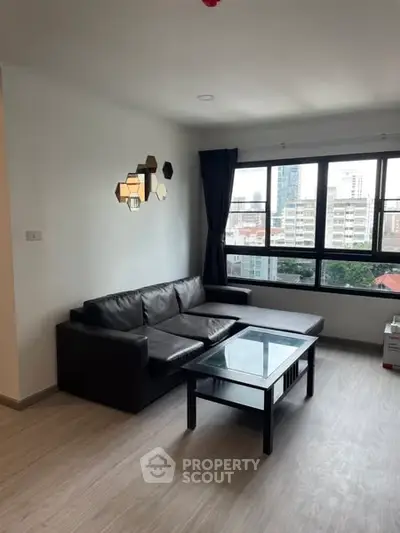 Modern living room with city view, featuring sleek black sofa and glass coffee table.