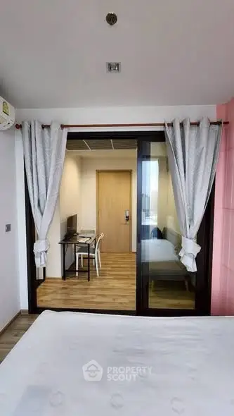 Modern bedroom with glass partition and study area, featuring elegant curtains and wooden flooring.