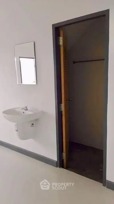 Minimalist bathroom with wall-mounted sink and mirror, featuring a small storage area.
