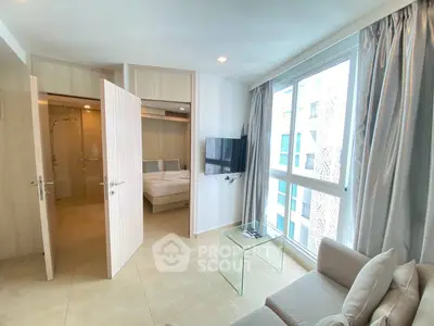 Modern living room with natural light and bedroom view, featuring sleek furniture and large windows.